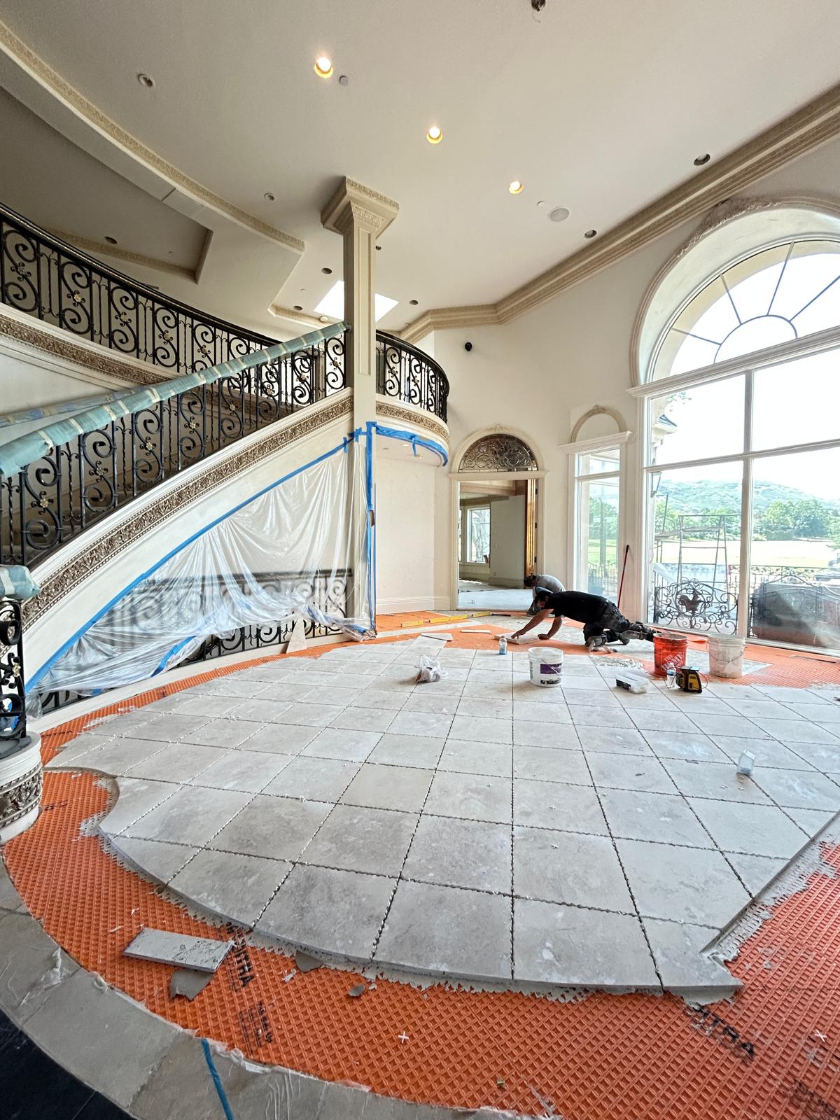 Natural stone tile flooring being installed in the two-story grand foyer beneath the curved staircase