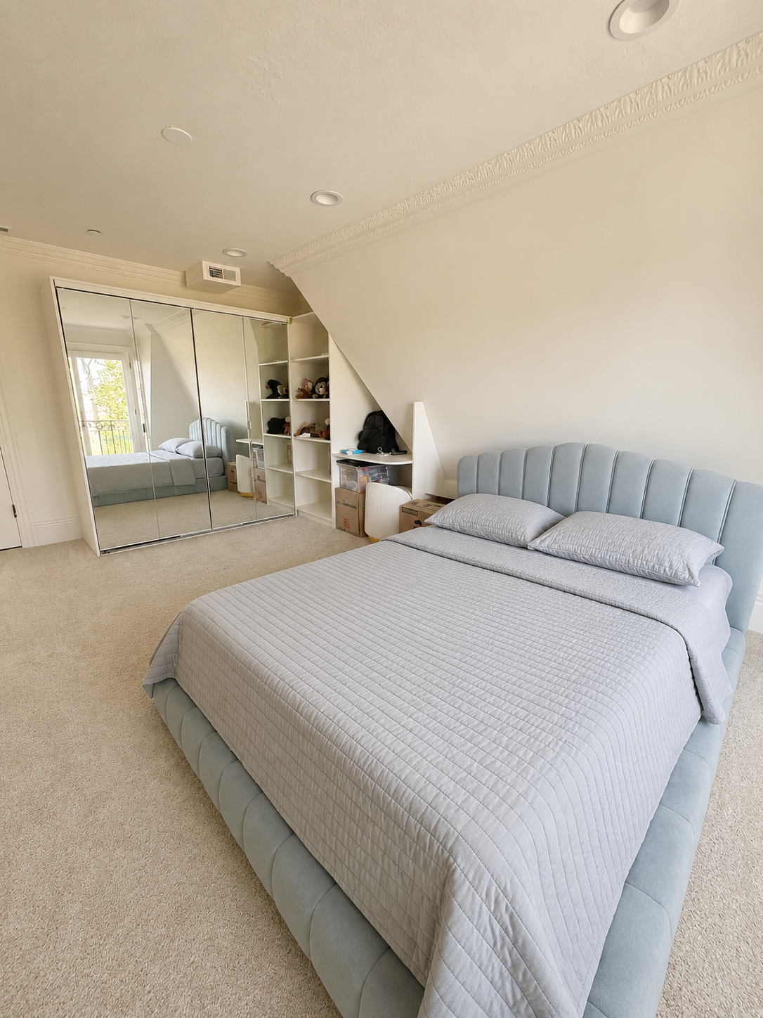 Completed upstairs bedroom with channel-tufted upholstered headboard, mirrored closet doors, and built-in shelving