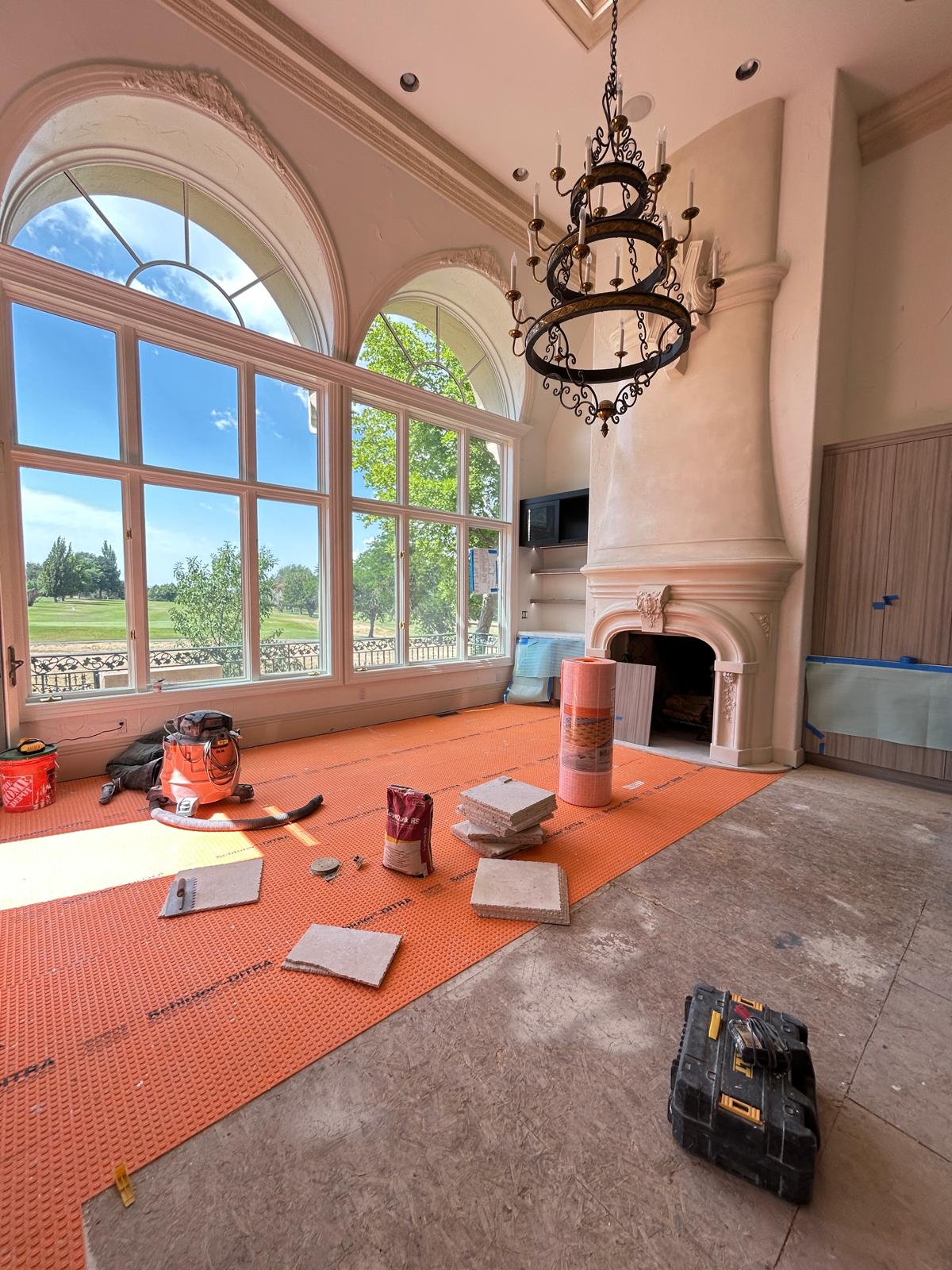 Two-story great room with arched windows, iron chandelier, and cast-stone fireplace during construction