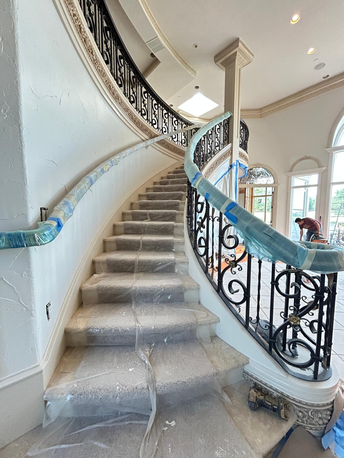 Sweeping curved staircase with hand-forged wrought iron railings and ornate scrollwork during construction